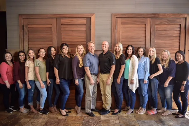 Staff members standing in a line and smiling together in front of wooden doors indoors.